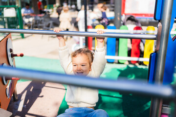 Fototapeta premium Smiling toddler playing and hanging from monkey bars at the playground