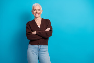 Senior woman with arms crossed smiling confidently against a vibrant blue background, embodying...