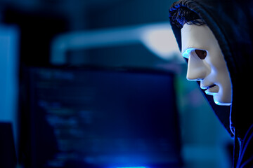 An anonymous computer hacker with a mask and hoodie writes malicious code to break into a secure...