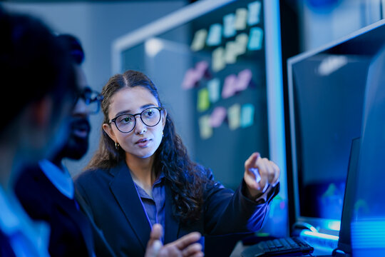 An agile development team participates in a sprint retrospective meeting. A female developer contemplates the user stories on the kanban board visible in the background.