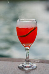 Copa de cóctel rojo con humo y rodaja de limón junto a la piscina