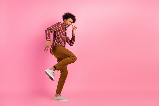 Young man dancing joyfully wearing stylish casual attire on a vibrant pink background showcasing playful energy