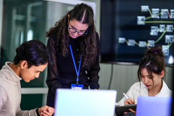 A female team leader mentors her junior IT staff in a tech office. The diverse group is working...