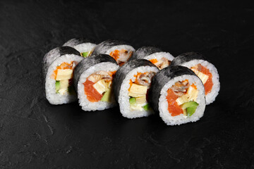Delicious sushi rolls with eel, salmon, avocado, and cream cheese filling on black background