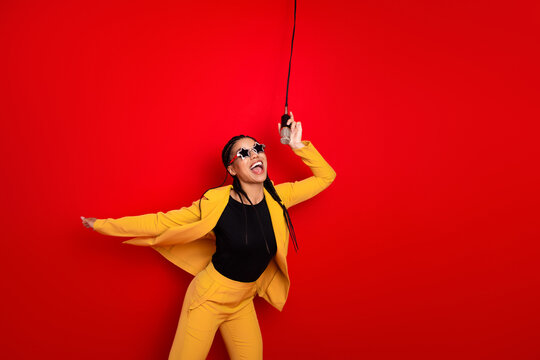 Cheerful woman in stylish yellow suit singing with microphone on red background in a vibrant and energetic pose.