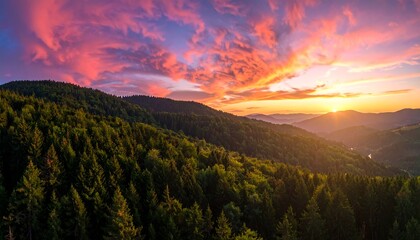 Obraz premium A breathtaking vista of a mountain range at sunset, showcasing a vibrant, colorful sky with a dramatic display of warm hues over lush, green forests.