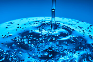 The viscous gel serum for the face flows and collects into a drop on a blue background..