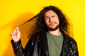 Young man with long black hair making a funny face and pulling his hair on yellow background