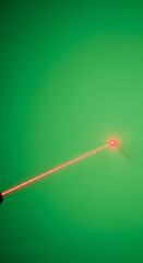 A red laser beam projects a bright point onto a uniform green backdrop.