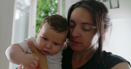 Mother kisses her baby on the cheek while holding them in her arms, creating a tender and loving...