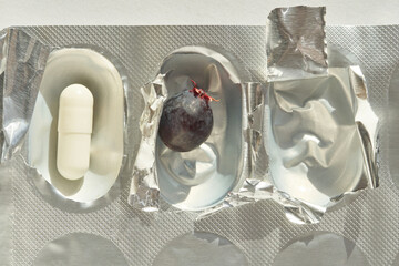 Contrasting elements of medicine and nature: capsule next to grape in metallic blister pack.