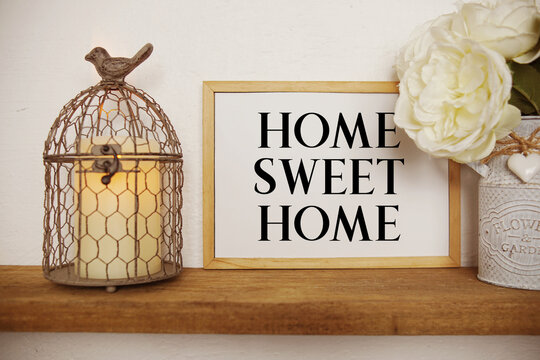 Home Sweet Home text written on whiteboard with LED candle light and bird cage on wooden shelf