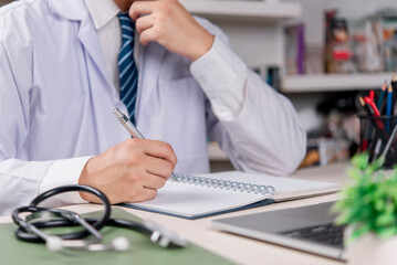 Doctor, healthcare Physician writes notebook at clinic office hospital document patient record, plan diagnosis and treatment, stethoscope and laptop, accurate medical paperwork and care quality.