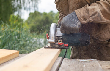 A man wearing gray gloves is cutting a board with a circular saw.
