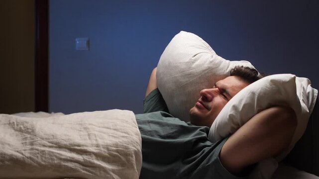 Man covering ears with pillow trying to sleep in bed