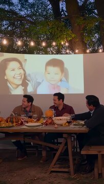 Close knit friends gathering in backyard garden, enjoying family slideshow during cozy evening dinner party with warm autumn atmosphere and festive fall decorations