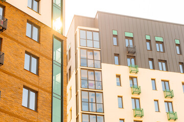 The facade of the residential complex combines brick and light finishing. Narrow windows, balconies with metal railings. Modern style, clear lines, contrasting materials.