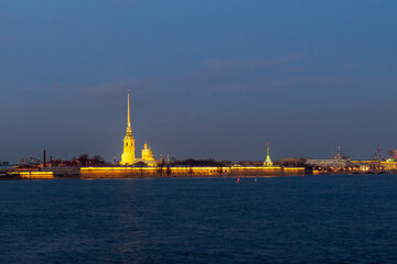 Fototapeta premium Twilight view of illuminated Peter and Paul Fortress with cathedral spire reflected in Neva River against darkening sky. Saint Petersburg, Russia.