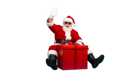 Cool santa claus wearing sunglasses sitting on a large red gift box waving hello isolated on transparent background