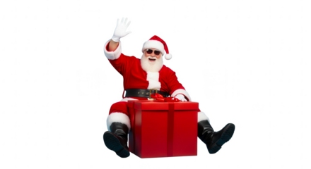 Cool santa claus wearing sunglasses sitting on a large red gift box waving hello isolated on transparent background