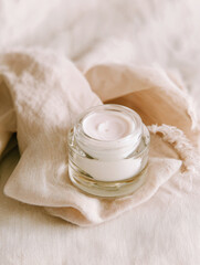 Cream glass jar with cosmetic product set on soft fabric in studio lighting