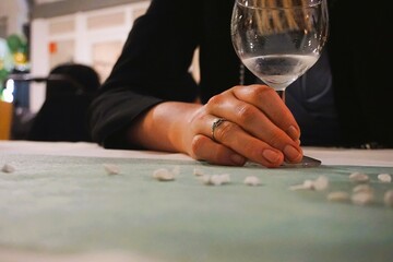 Junge attraktive Frau mit blonden langen Haaren und schwarzem Oberteil sitzt vor festlich gedecktem Tisch und umfasst leeres Weinglas auf Feier am Abend 