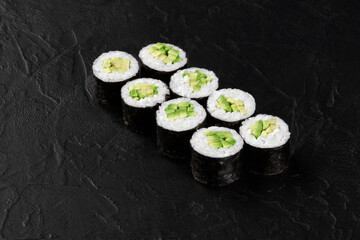 Eight sushi rolls with avocado filling resting on black slate surface