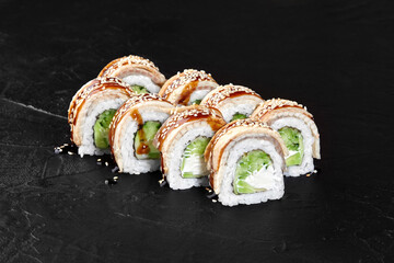 Dragon rolls with eel, avocado, cream cheese and sesame seeds resting on dark stone surface