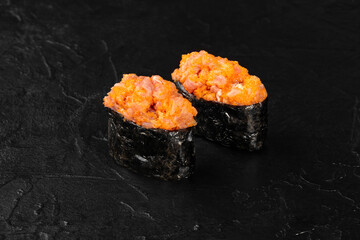 Gunkan maki sushi with spicy tuna and tobiko on black stone background