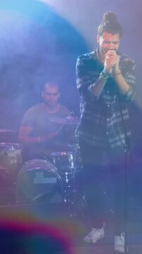 Animation of glowing blue lights over caucasian man singing with band playing on stage