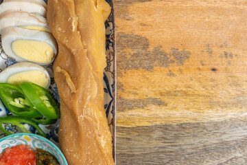 Yemenite Jewish pastry Jachnun served with pepper sauce, mashed tomatoes, boiled eggs on traditional platter over wooden background. Free space for text.
