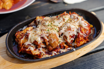 Spicy chicken and vegetable stir-fry with melted cheese on a hot skillet, presented on a wooden board.