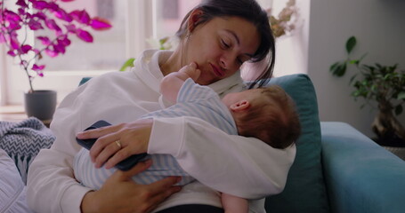 Obraz premium Mother holding her baby on the couch, her face showing both calm and fatigue, reflecting the daily reality of motherhood, in a comfortable and peaceful home setting-SD 480p