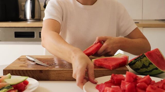 In a sunny kitchen, a woman methodically cuts a ripe watermelon into neat slices. She uses a sharp knife and focuses on creating manageable portions, showcasing her technique