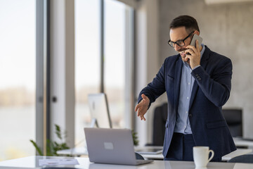 Businessman talks on phone while presenting ideas in modern office with laptop