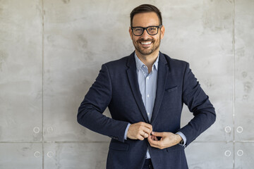 Business professional adjusts jacket while smiling in modern office setting with concrete wall during daytime