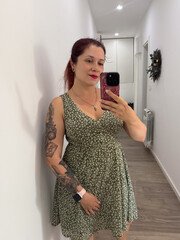 Woman taking mirror selfie in green floral dress with tattoos. Personal style, lifestyle, fashion and self expression with beauty, identity and appearance.