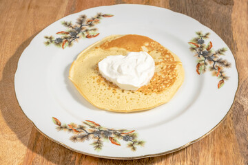 Plate and pancake on it served with sour cream in the form of heart. Food for Butter Week.
