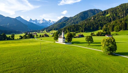A bird's-eye view of a church nestled in a vibrant green valley, framed by rolling hills and towering mountain peaks, illuminated by bright sunlight
