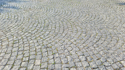 Fototapeta premium Close-up view of a cobblestone pavement featuring curved patterns, overgrown with grass. This textural shot highlights the beauty of stone pathways in urban settings, showing wear and nature.
