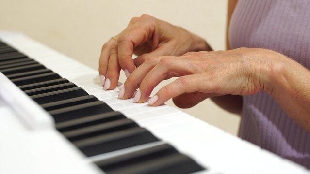 Hands Piano Keyboard Playing Music Lesson: Close-up view of woman's hands playing a digital piano keyboard during a music lesson.