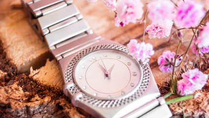 Elegante reloj plateado con flores rosas sobre superficie de madera