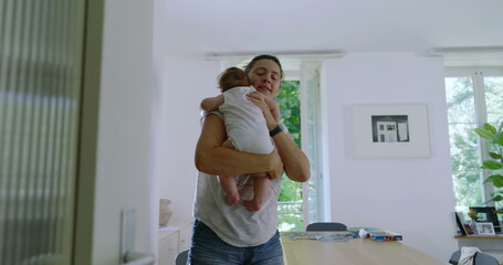 Mother holding her baby while walking through a home corridor, depicting an authentic family moment...
