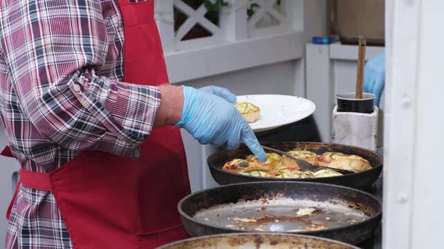 The cook puts the national Udmurt dish into a plate from a frying pan - perepechi at the festival of cuisines of small peoples of Russia.