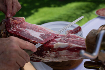 Close-up of a traditional Spanish jamón being sliced by hand at an outdoor event.
