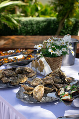 Fresh oysters and mussels on ice at an outdoor seafood buffet with lemon wedges and flowers in a tropical garden setting.