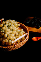 Fresh ripe grapes in a woven basket with a background of dark grapes and wooden spoon