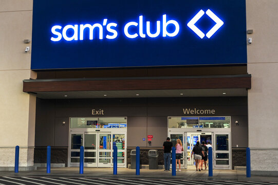 Sam's Club retail warehouse entrance with illuminated signage and customers entering, representing wholesale shopping and bulk merchandise operations.
