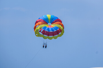 Brightly colored parasail with two people enjoying thrilling parasailing in a sunny blue sky. Outdoor water sport adventure, summer vacation.