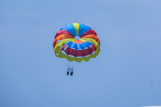 Brightly colored parasail with two people enjoying thrilling parasailing in a sunny blue sky. Outdoor water sport adventure, summer vacation.
